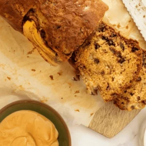 A loaf of Cardamom Coffee Banana Bread with a golden-brown crust and a moist, spongy interior, sprinkled with a light dusting of cardamom powder.