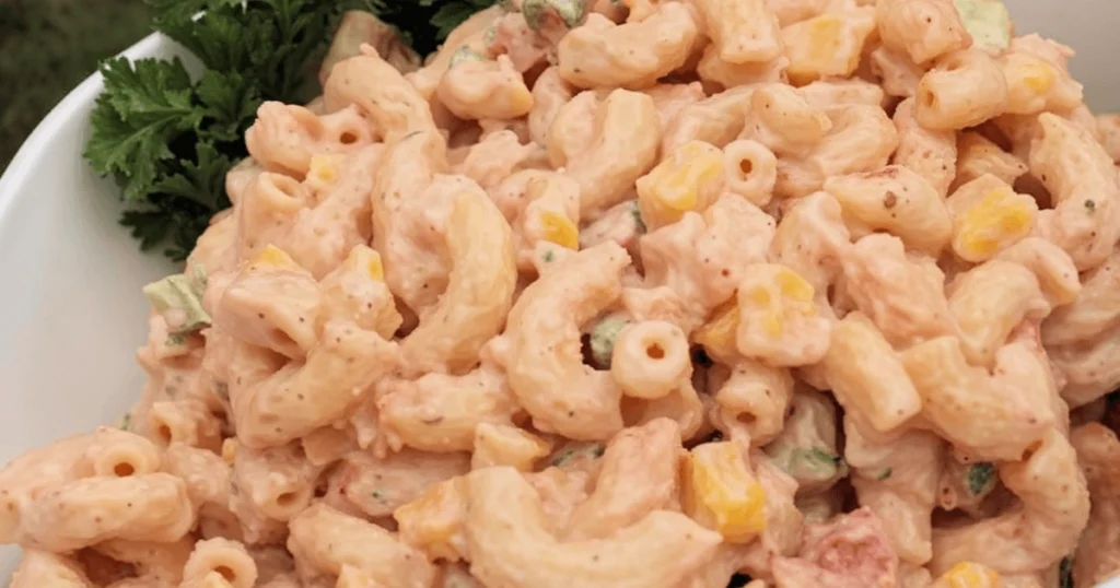 Creamy macaroni salad with corn, green herbs, and a smoky dressing served in a white bowl, ready to be enjoyed at a summer party.