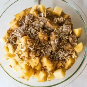A glass bowl filled with diced potatoes coated with Lipton onion soup mix and seasonings, ready for roasting or baking.