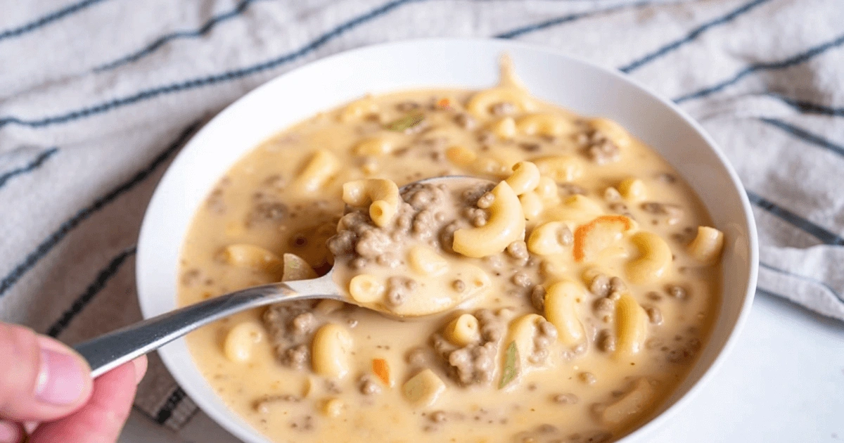 A close-up of a bowl filled with creamy cheeseburger macaroni soup, featuring ground beef, elbow macaroni, and a rich cheese-based broth, with a spoon scooping up a bite.