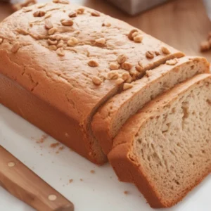 A golden loaf of Pineapple Banana Bread on a wooden cutting board, topped with fresh banana slices and pineapple chunks, ready to be sliced and served.