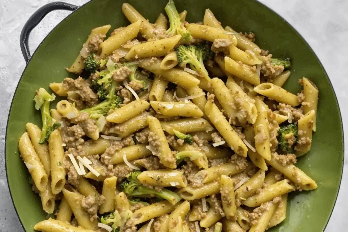 A close-up of penne pasta with ground beef, broccoli, and Parmesan cheese in a green bowl.