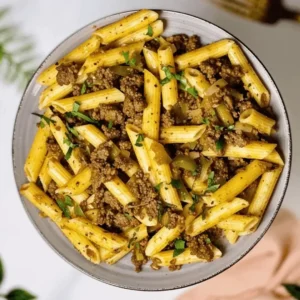 A bowl of seasoned penne pasta with ground beef, onions, and fresh herbs.