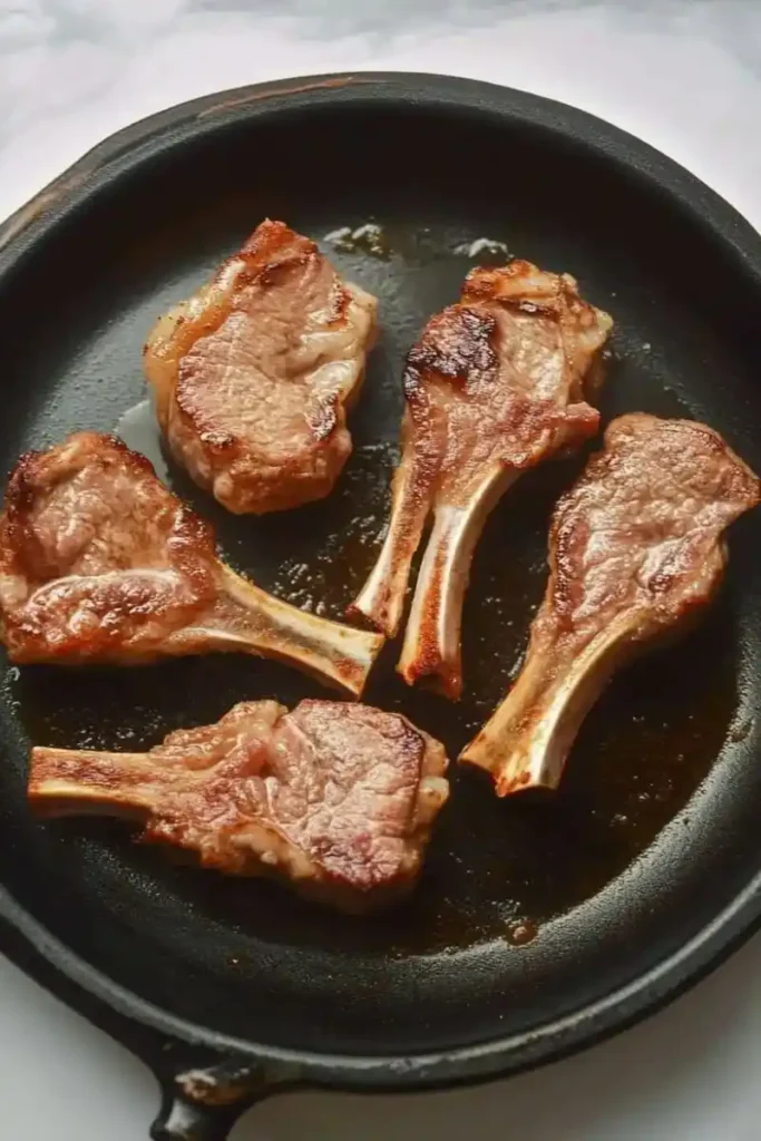 Pan-seared lamb lollipops cooking in a cast iron skillet.