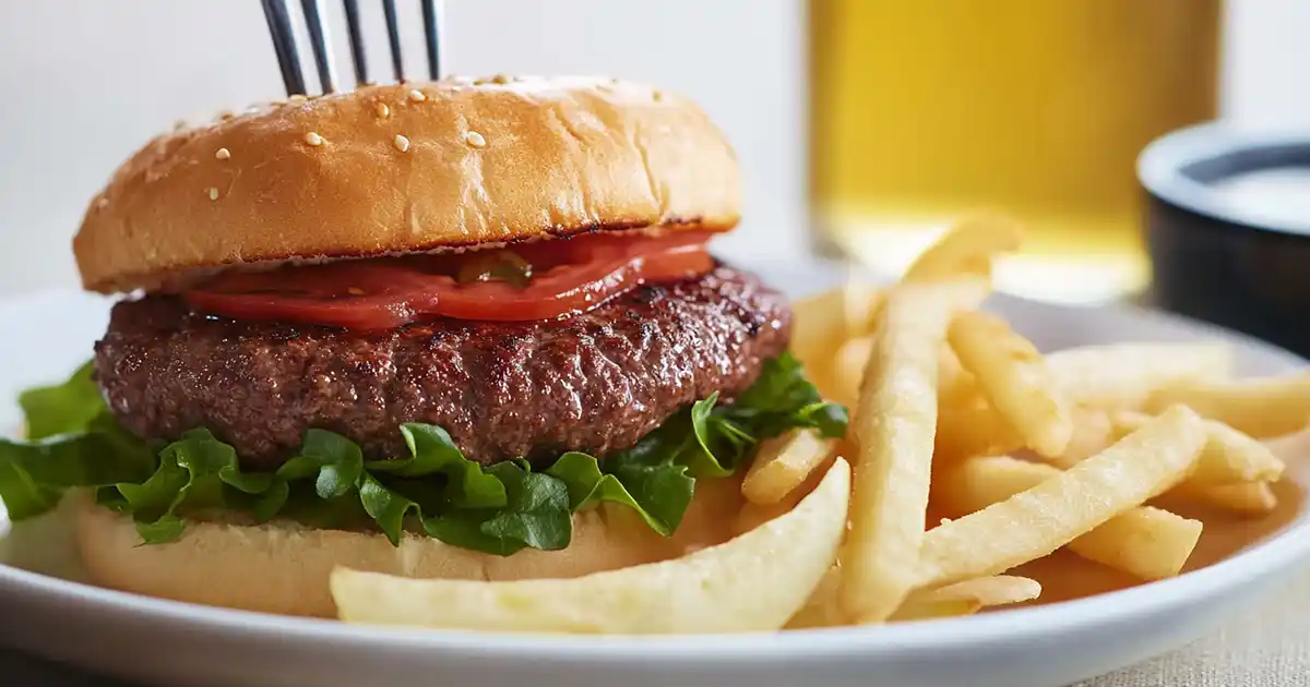 A grilled Wagyu ground beef recipe (burger) with lettuce, tomato, and a toasted sesame seed bun, served with crispy fries.
